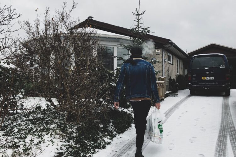 woman carrying plastic bag walking near house during winter